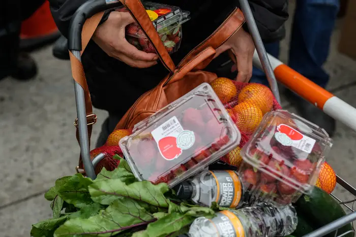 A shopping cart is full of fresh produce, including oranges, strawberries and Swiss chard.